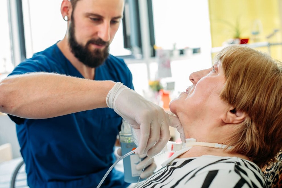 Pflegefachkraft schließt Inhalation an Trachealkanüle an Männliche Pflegefachkraft schließt eine Inhalation an eine Trachealkanüle an